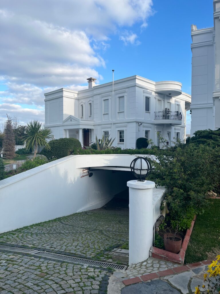Stunning white mansion surrounded by lush greenery under a clear blue sky.