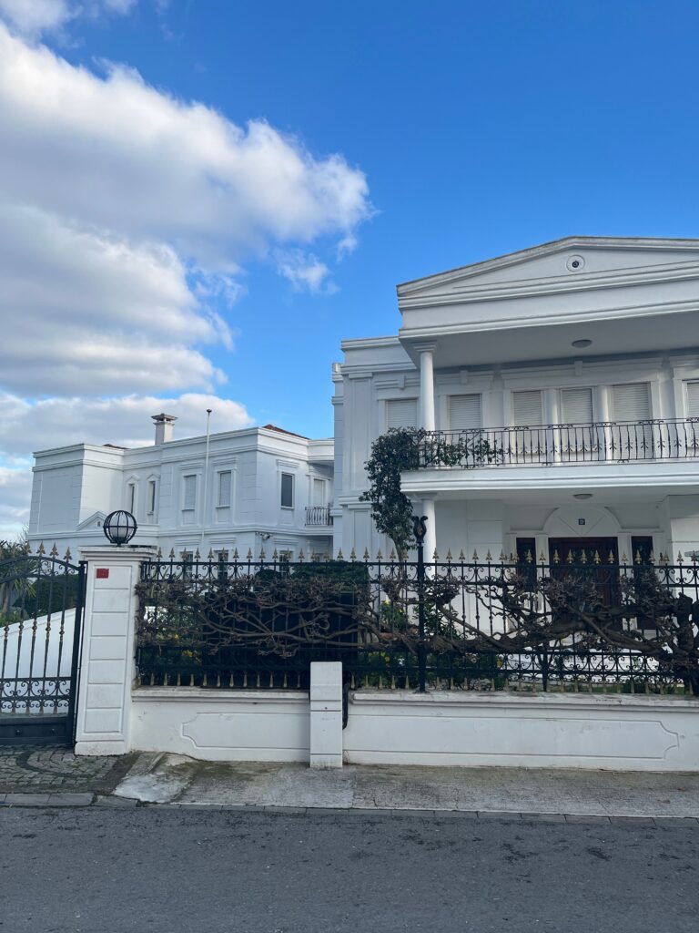 Beautiful white mansion with wrought iron fence under clear blue sky.